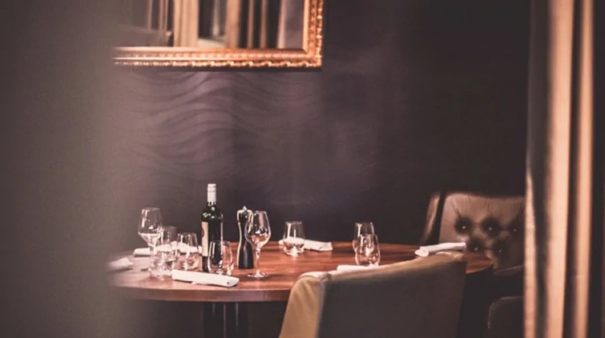 Gedeckter runder Tisch mit Weinflasche und Kristalllüster im Gastraum des Abacco's Steakhouse