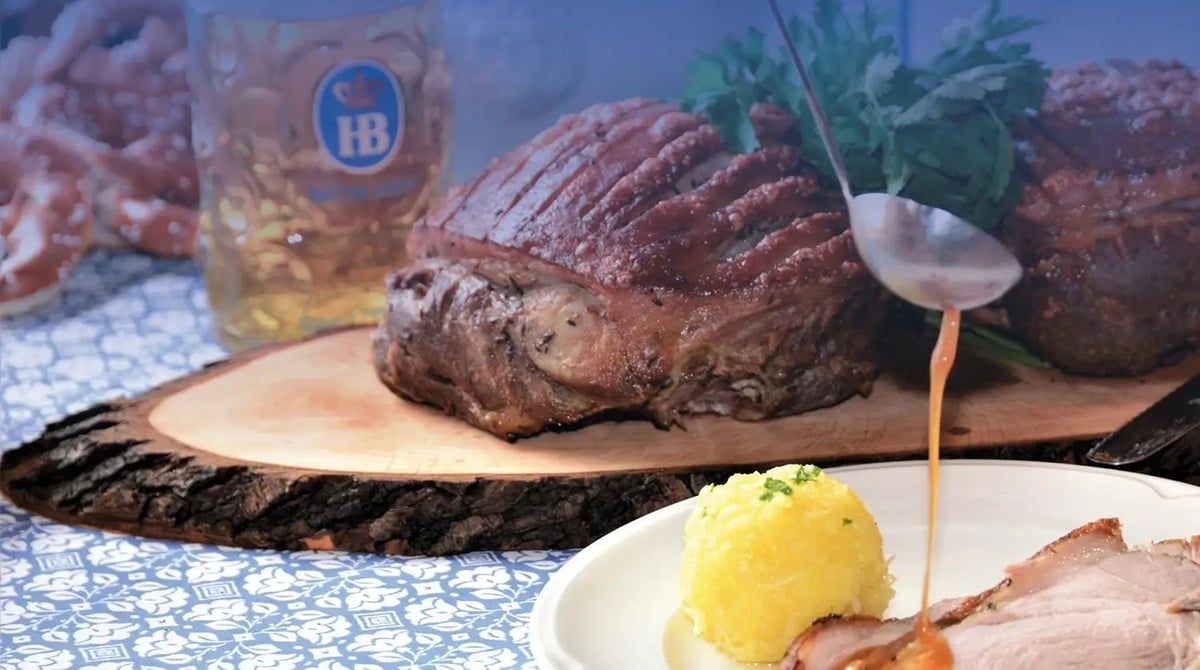 Krustenschweinebraten mit Kartoffelknödel und Soße, dahinter ein Maßkrug mit HB-Logo