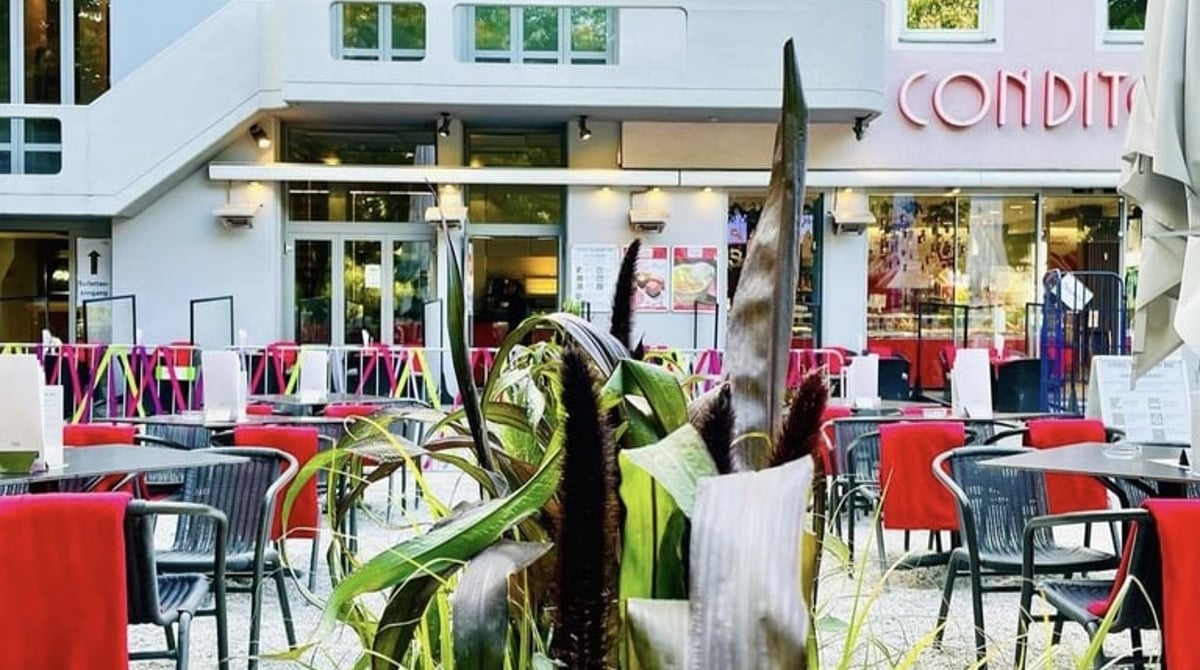 Die Terrasse des Café Münchner Freiheit mit Tischen und roten Tischdecken vor dem Haus mit Konditorei-Schriftzug