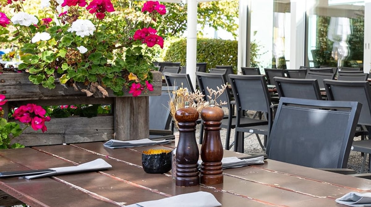 Gedeckter Terrassentisch mit Pfeffermühlen unter einem Sonnenschirm mit Blumen
