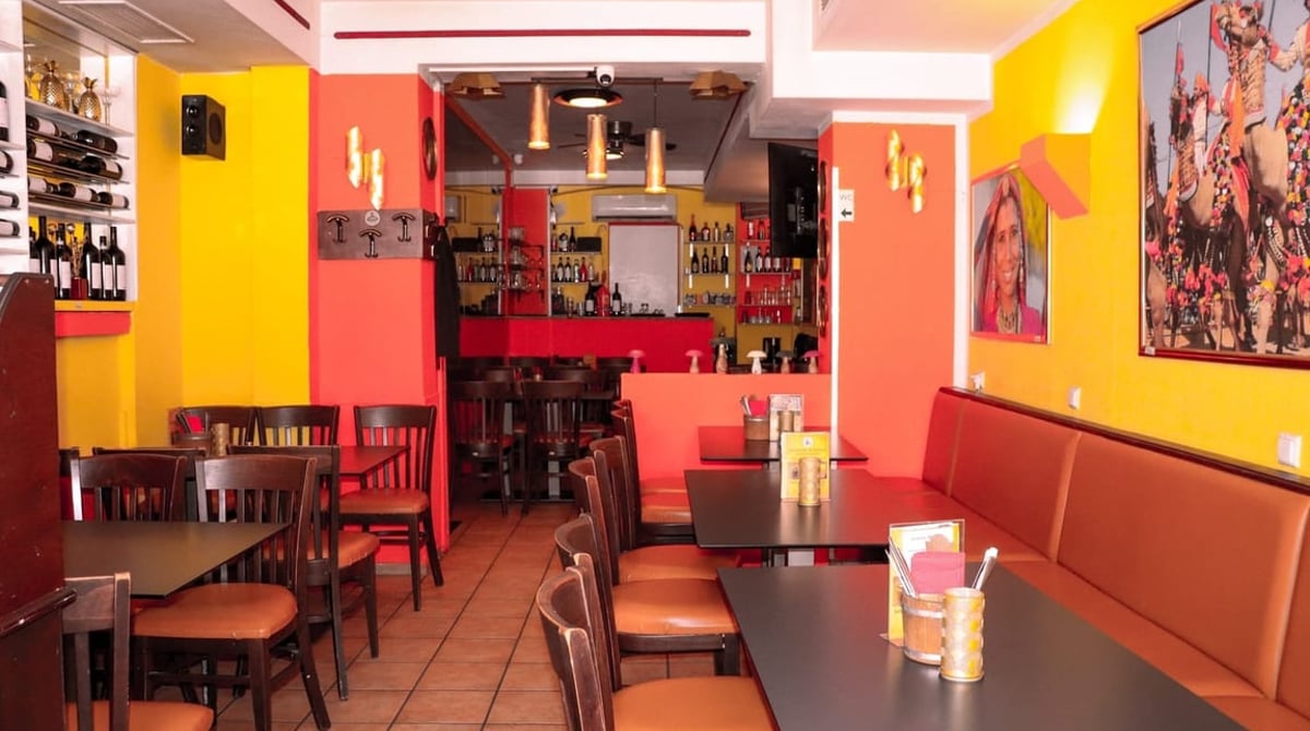 Gastraum des Indian Mango in München mit gelben und roten Wänden, Wandbildern, Holztischen und Bar im Hintergrund