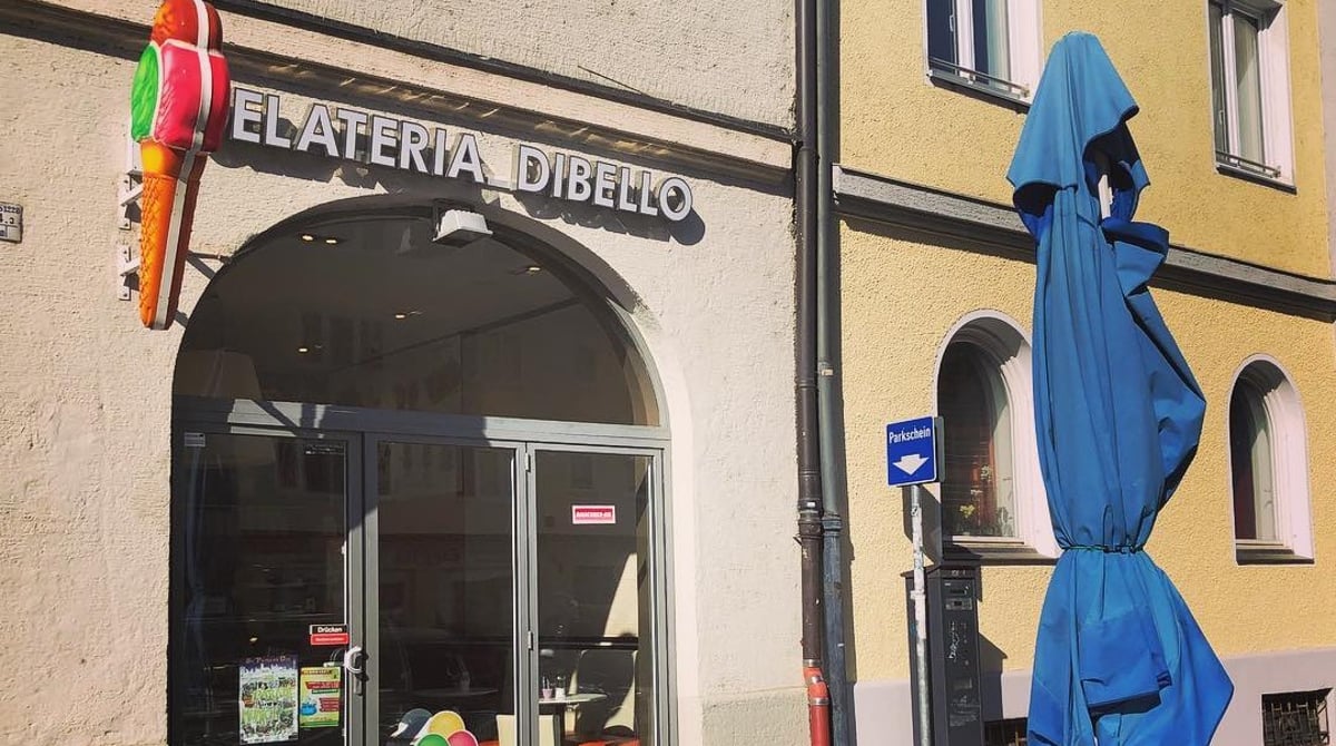 Eingang der Gelateria Dibello in Untergiesing mit Eiswaffel-Leuchtreklame und Tischen vor dem Haus