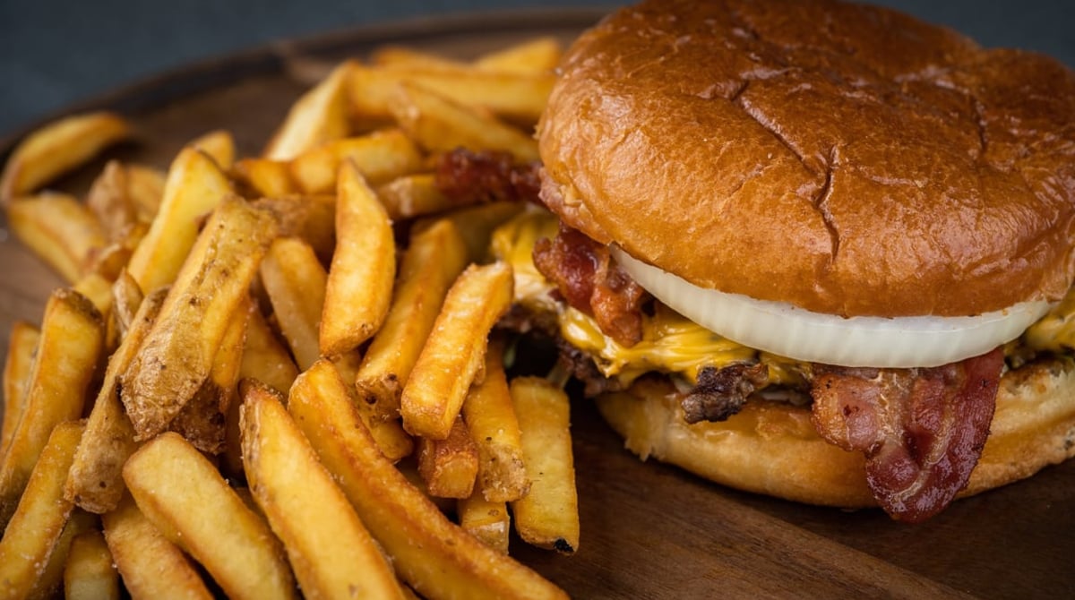 Cheeseburger mit Bacon und Zwiebelring neben Pommes auf einem Holzbrett