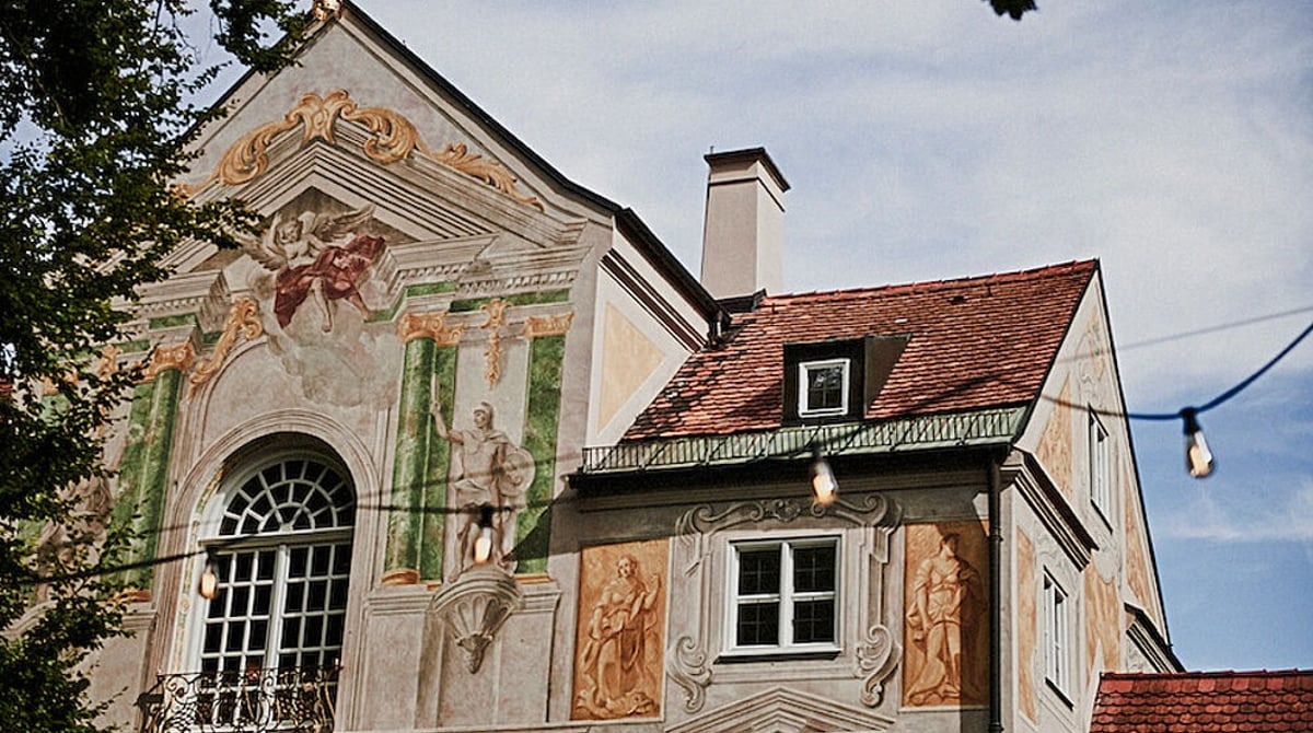 Außenansicht des Asam Schlössl mit bemalter Fassade und Lichterkette