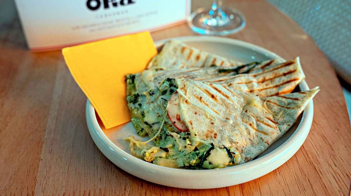 Gegrillte Piadina mit Spinat und Käse auf einem Teller, dahinter die Karte mit ORA-Logo