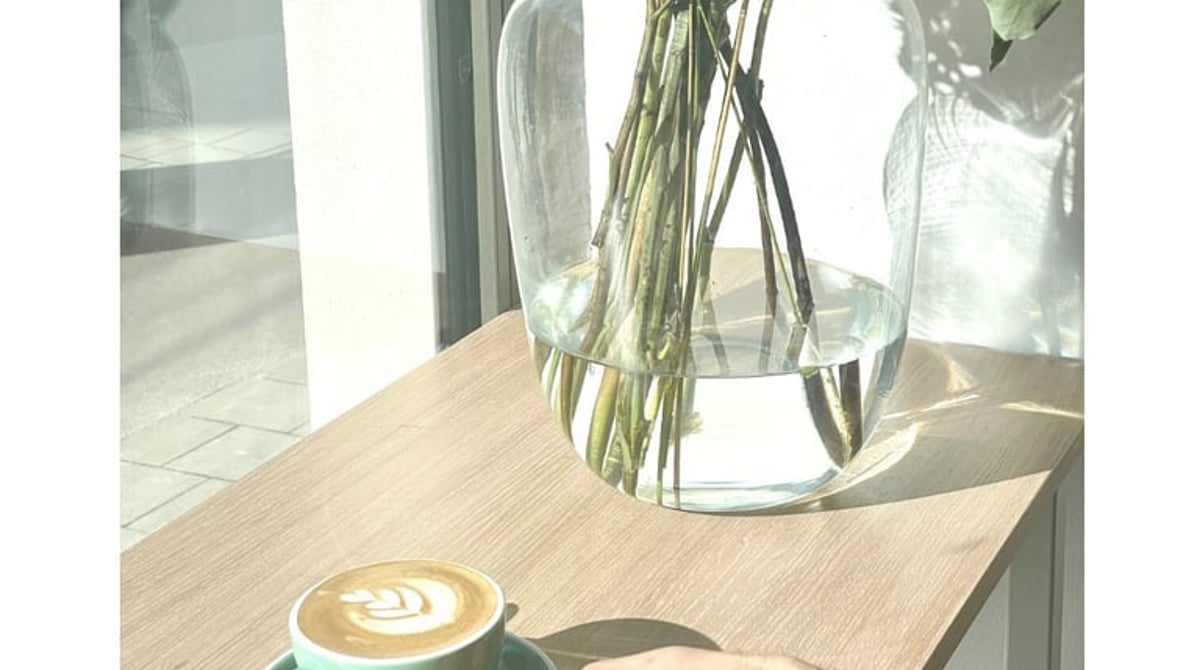 Kaffee mit Latte Art in einer grünen Tasse am Fenster neben einer Glasvase