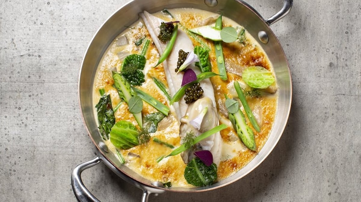 Fisch in goldgelber Sauce mit grünem Gemüse und Kaviar in einer Kupferpfanne