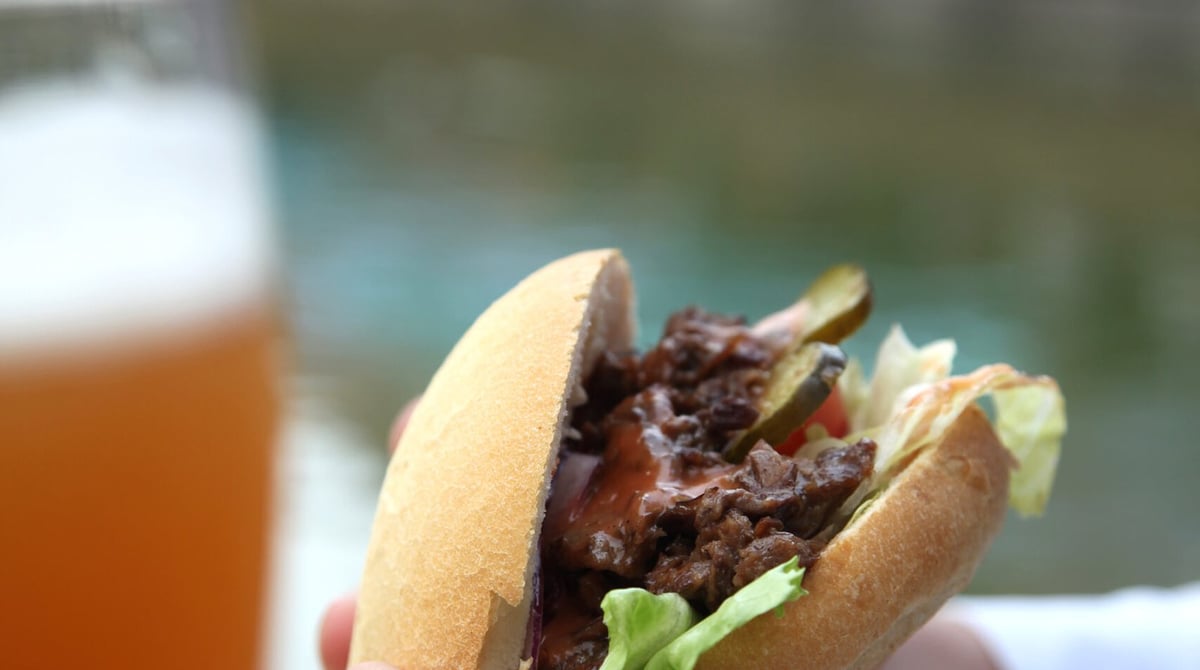 Zwei Hände halten eine mit Ochsenfleisch belegte Semmel