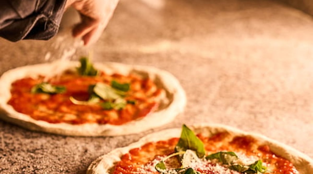 Zwei frisch belegte Pizzen auf der Arbeitsfläche vor dem Ofen