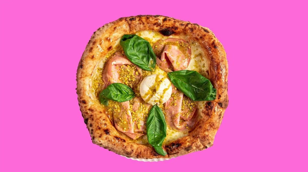 Pizza mit Schinken, Basilikum und Mozzarella, aufgeschnitten auf pinkem Hintergrund