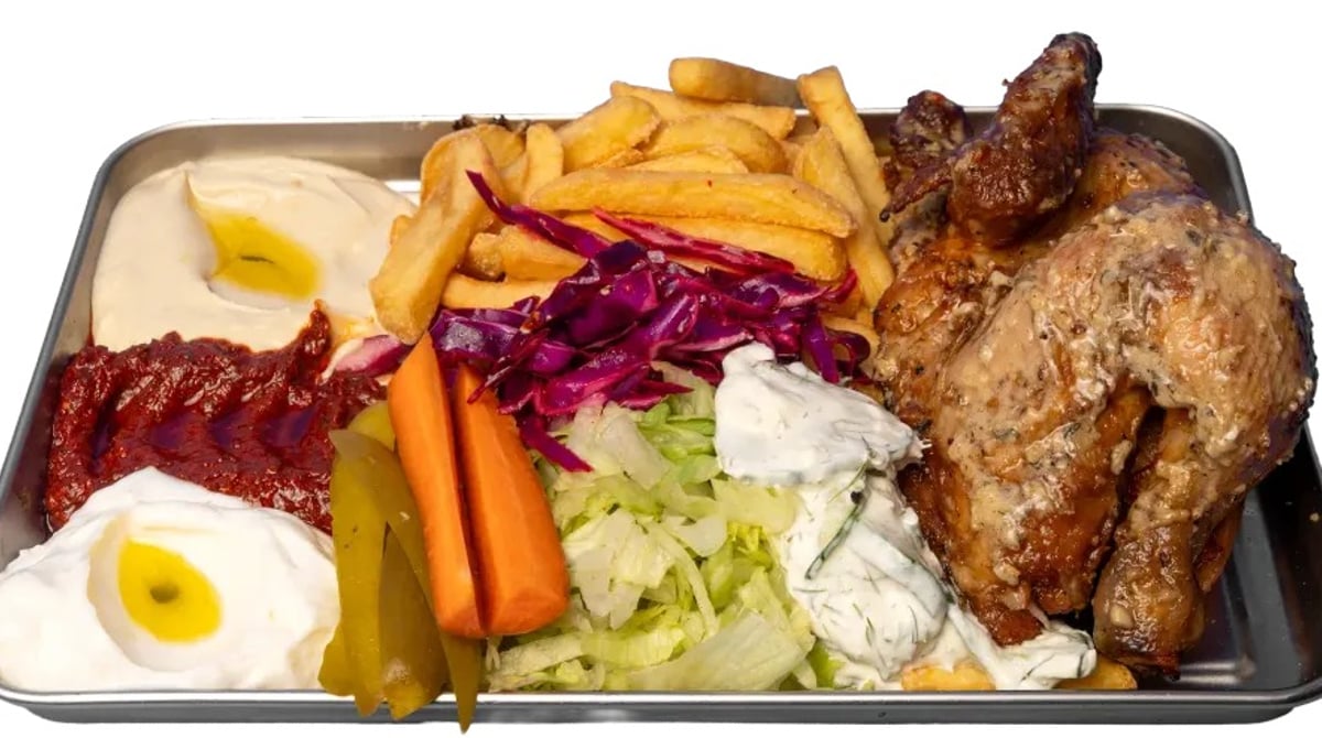 Hähnchen-Menü der Shawarmery auf einem Metalltablett: halbes Grillhähnchen, Pommes, Rotkohl, Salat, Karotten, Pickles und mehrere Dips