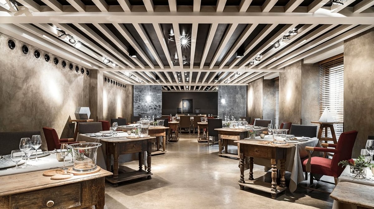 Gastraum des Restaurants Atelier im Bayerischen Hof mit Holztischen, Betonboden und Balkendecke