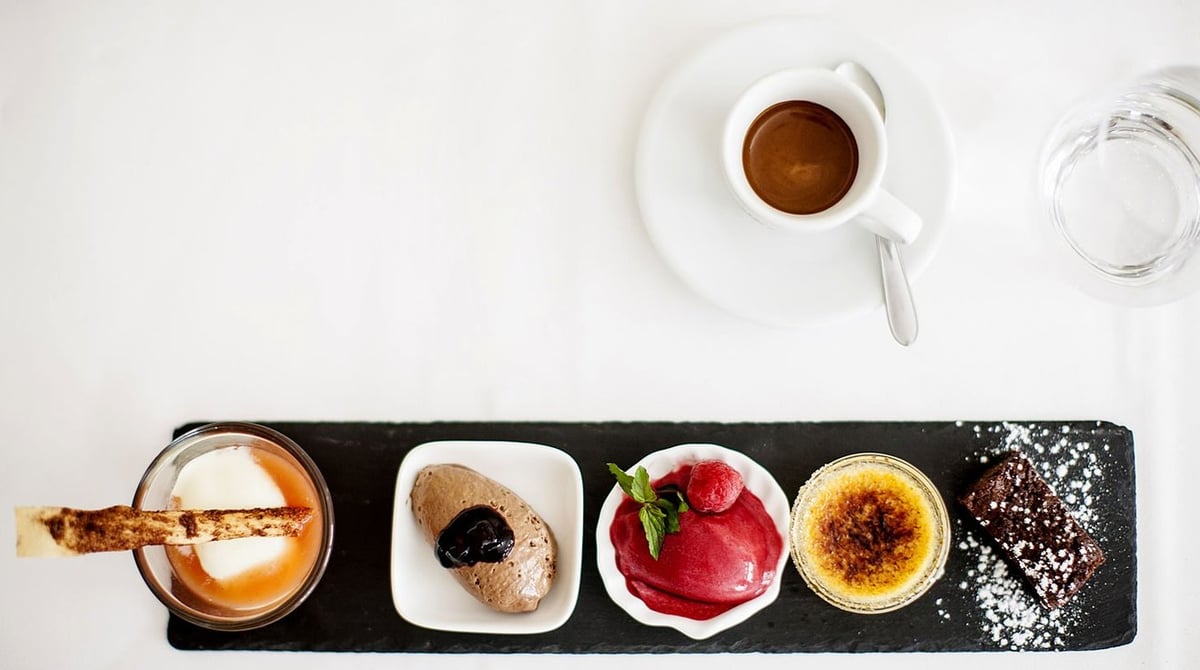 Dessertvariation mit Crème brûlée und Mousse auf Schieferplatte neben einem Espresso