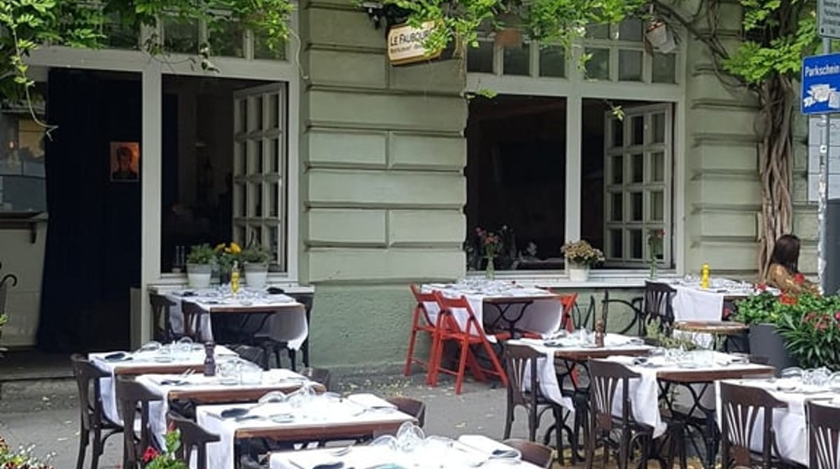 Terrasse des Le Faubourg mit weiß eingedeckten Tischen und Blumenkästen vor der begrünten Hausfassade