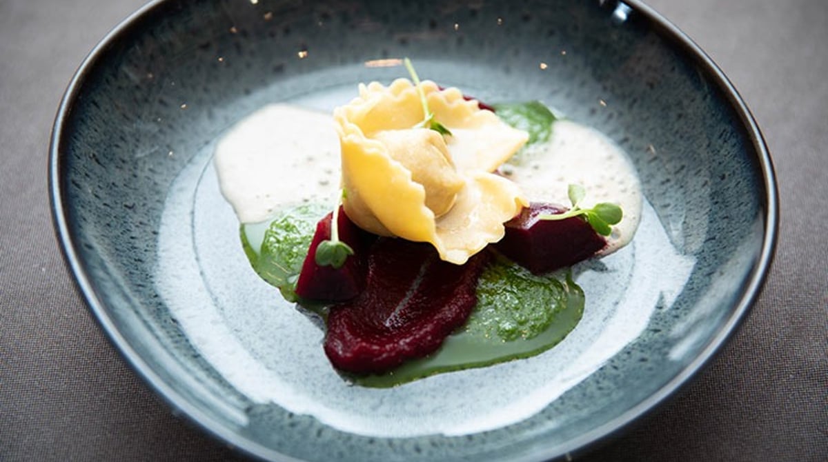 Gefüllte Teigtasche mit Roter Bete und grüner Creme in einer blauen Schale