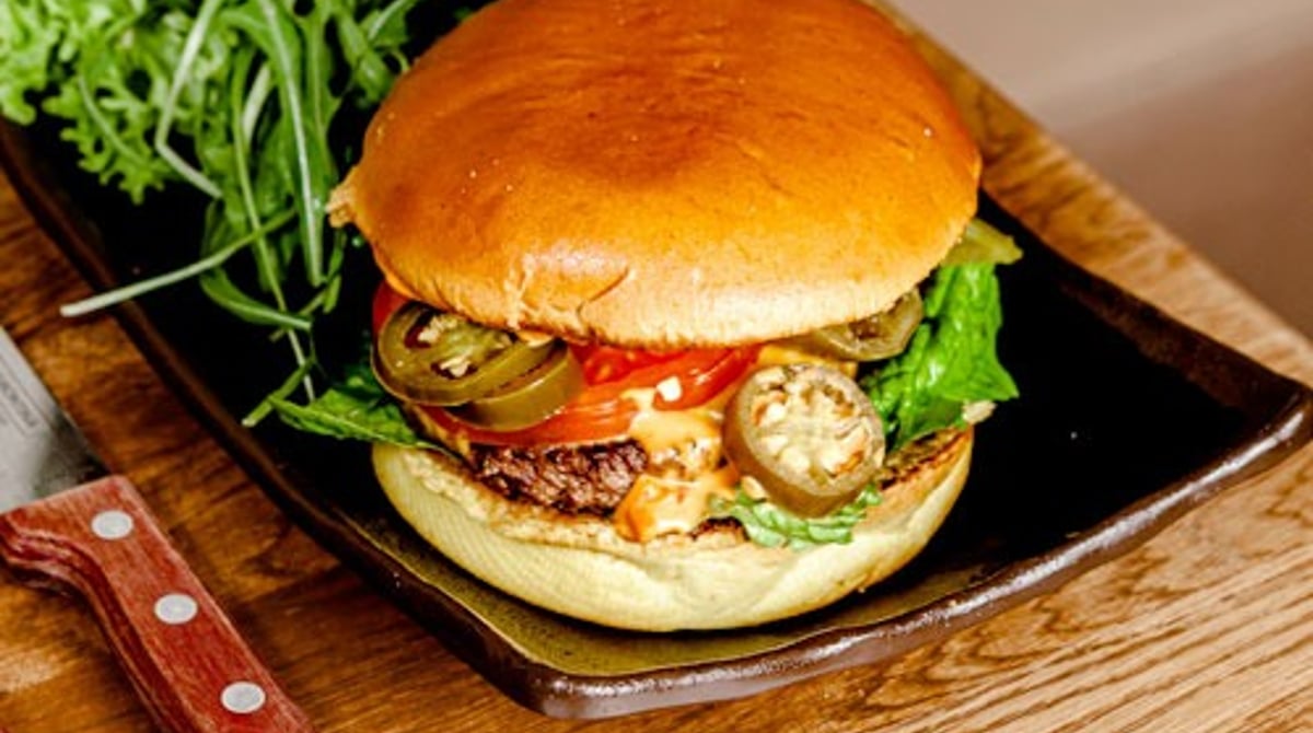 Burger mit Jalapeños, Rucola und Tomate auf einem Holzbrett bei King Loui
