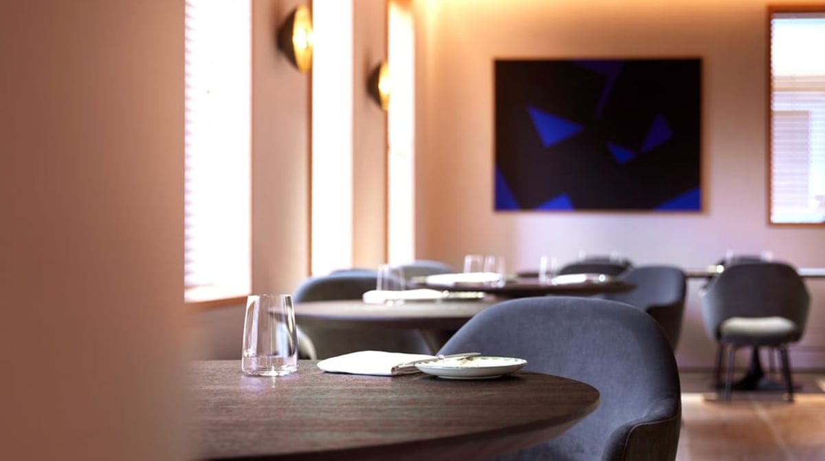 Gastraum des Restaurants JAN mit runden Holztischen, Stühlen und Blick in die offene Küche