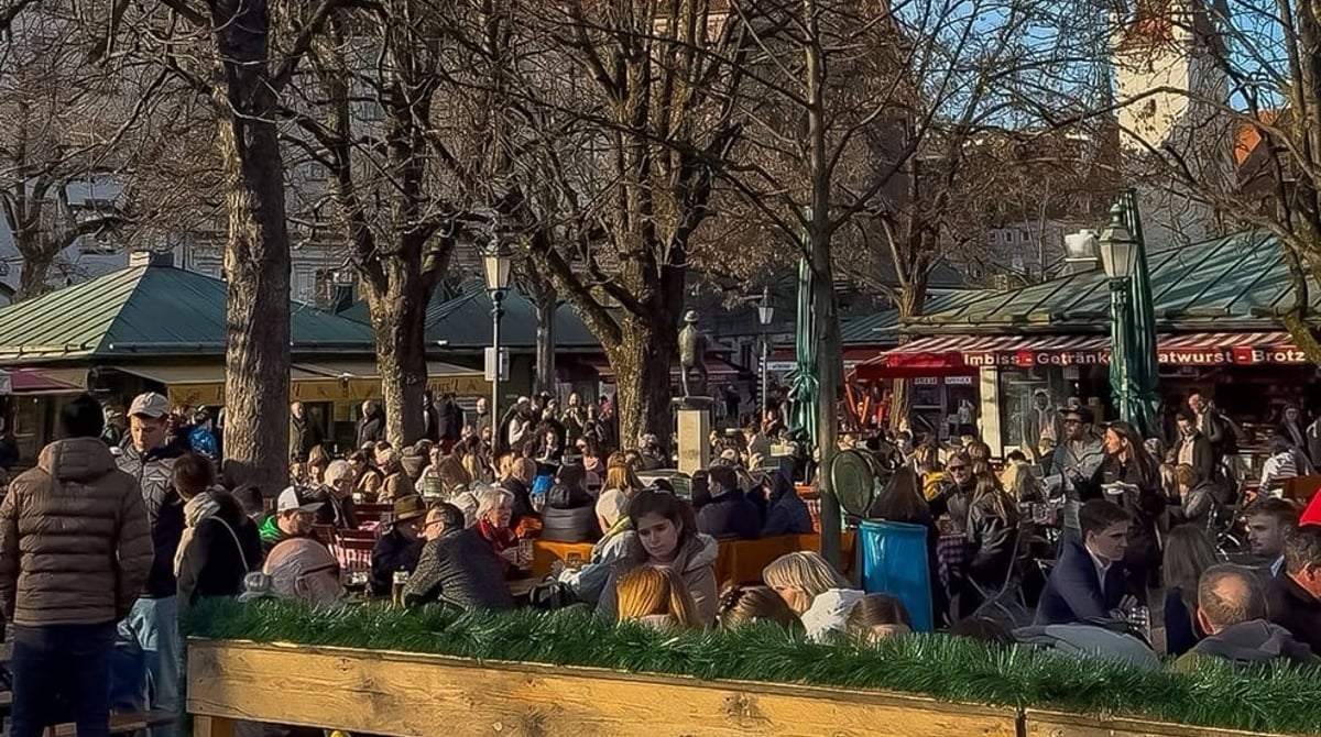 Gäste im Biergarten am Viktualienmarkt, im Hintergrund ein Kirchturm