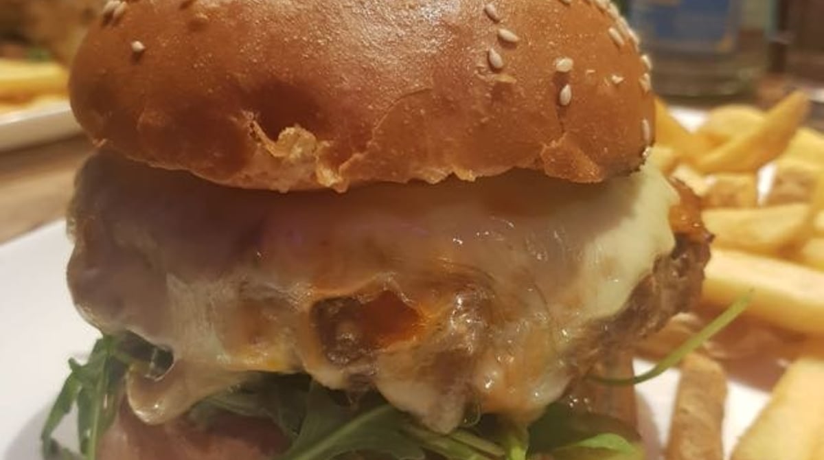 Burger mit geschmolzenem Käse und Rucola im Sesambrötchen, daneben Pommes