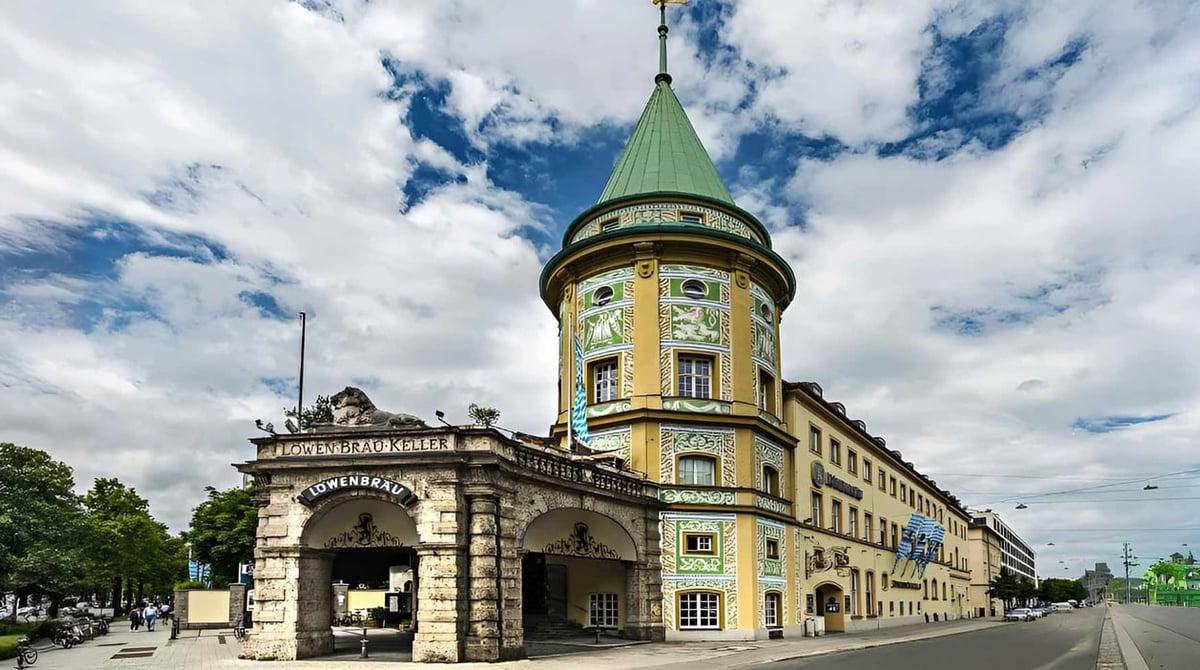 Der Löwenbräukeller am Stiglmaierplatz in München mit Turm und grünem Dach unter bewölktem Himmel