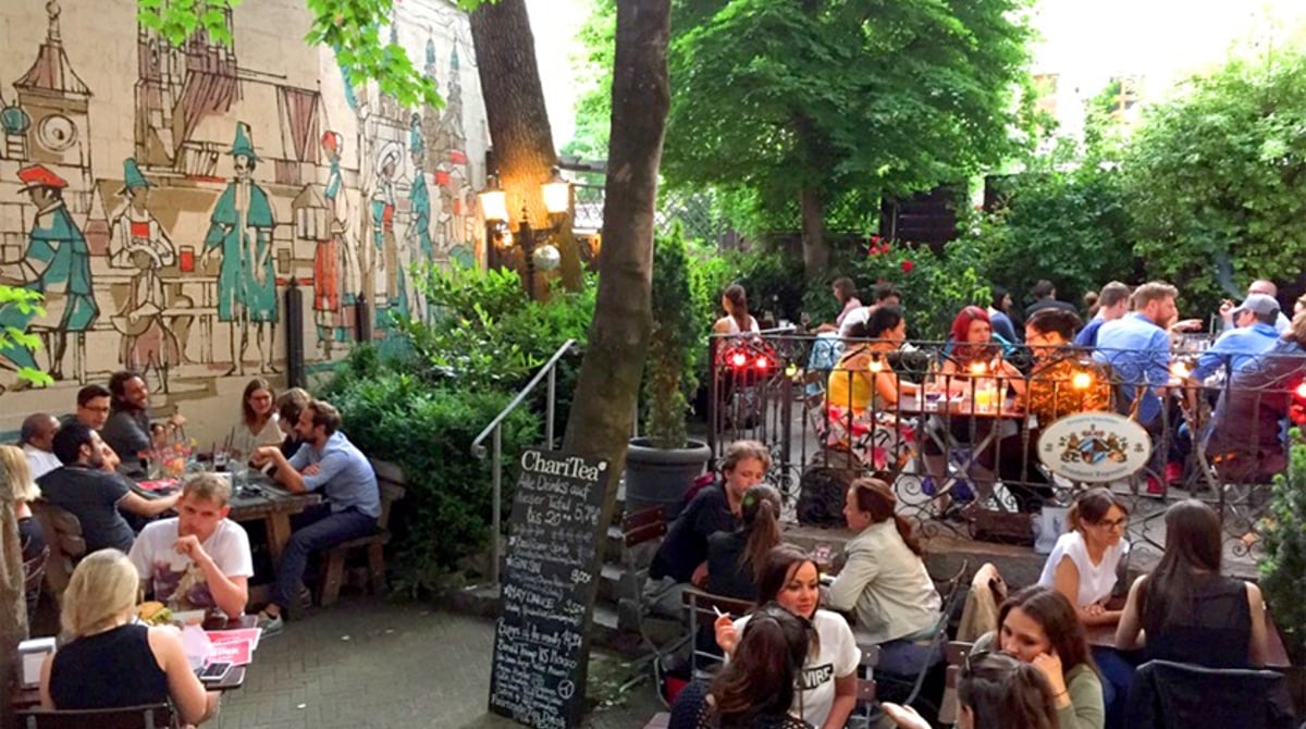Biergarten im Innenhof des M.C. Müller mit Bäumen, Wandmalerei und vollen Tischen