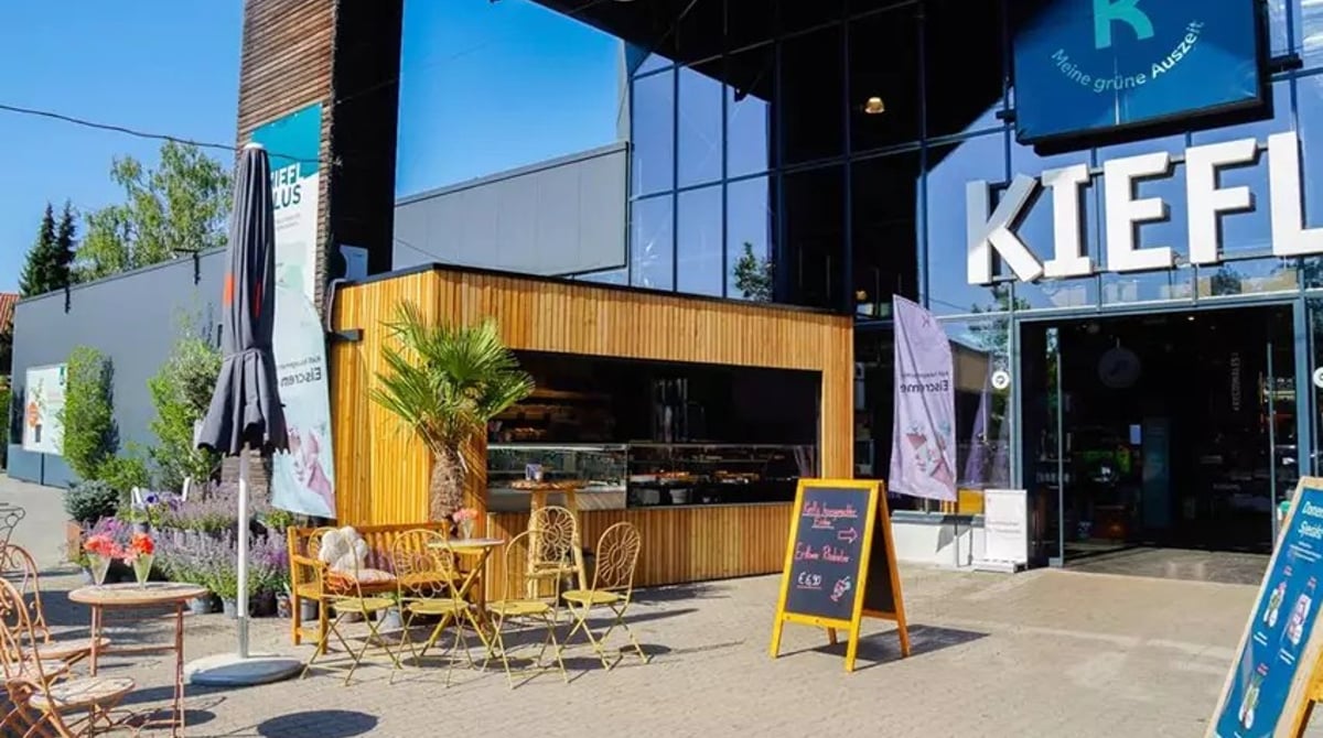 Außenansicht der Kiefl To-Go-Bar mit Holzfassade, Bistrostühlen und Eingang zum Gartencenter