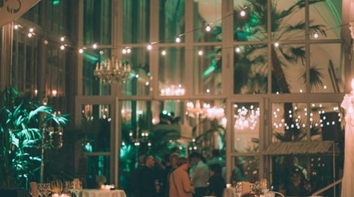 Abendlich beleuchteter Gastraum im Palmenhaus mit hohen Rundbogenfenstern und Palmen