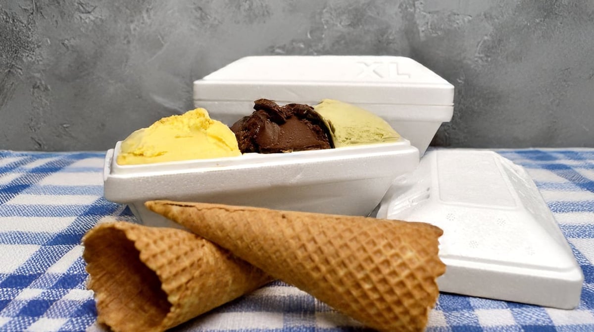 To-go-Box mit drei Sorten Eis, daneben zwei Waffeln auf einem karierten Tuch