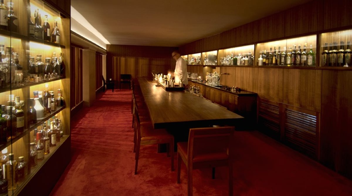 Barraum des Les Fleurs du Mal mit langem Tisch und beleuchteten Flaschenregalen