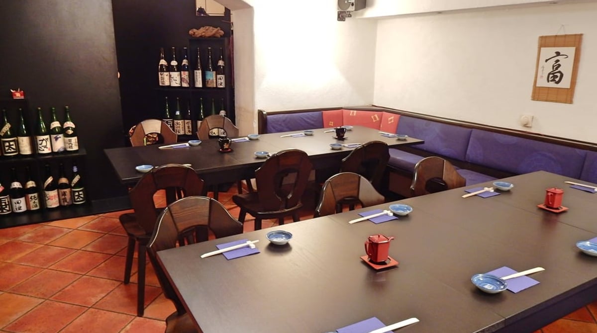 Gastraum des Kaito mit dunklen Holztischen, Sitzbank und Regalen mit Sake-Flaschen