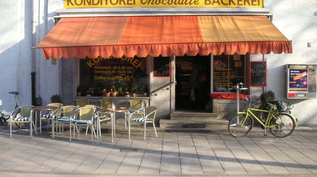 Außenansicht der Konditorei und Bäckerei Chocolatte an der Prinzregentenstraße mit orangefarbener Markise und Tischen davor