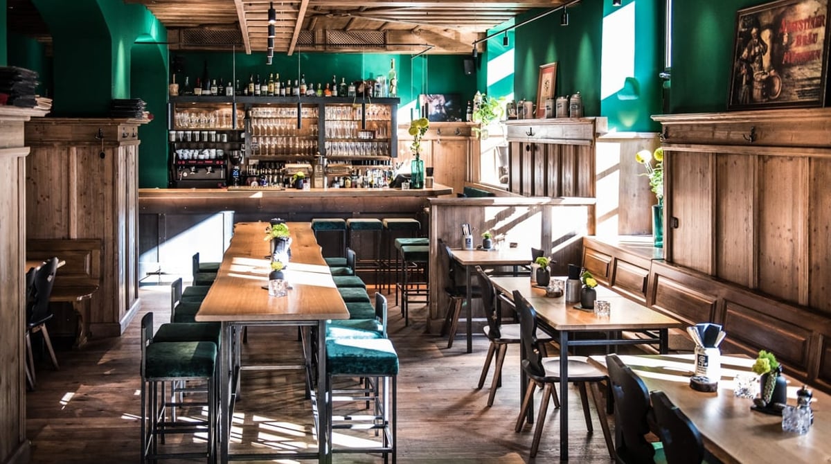 Gastraum des Xaver's mit grünen Wänden, Holzvertäfelung, Bar und langem Holztisch