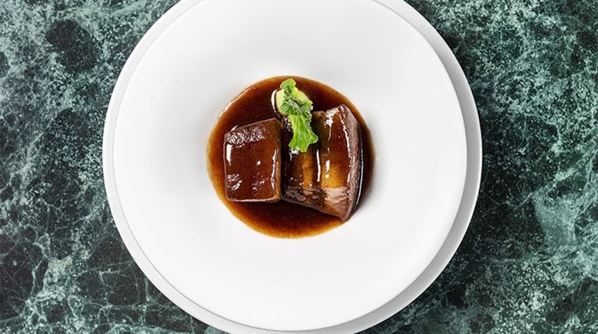 Geschmorte Schweinebauch-Stücke mit dunkler Sauce auf einem weißen Teller