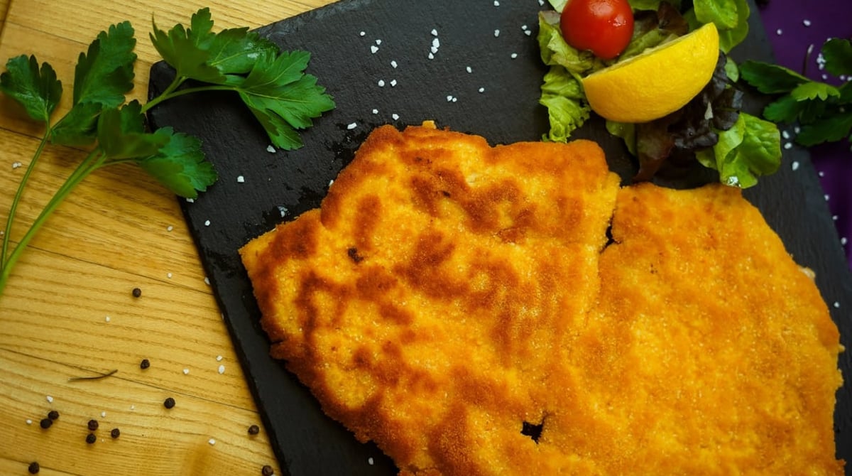 Paniertes Schnitzel mit Salat und Zitrone auf einer Schieferplatte