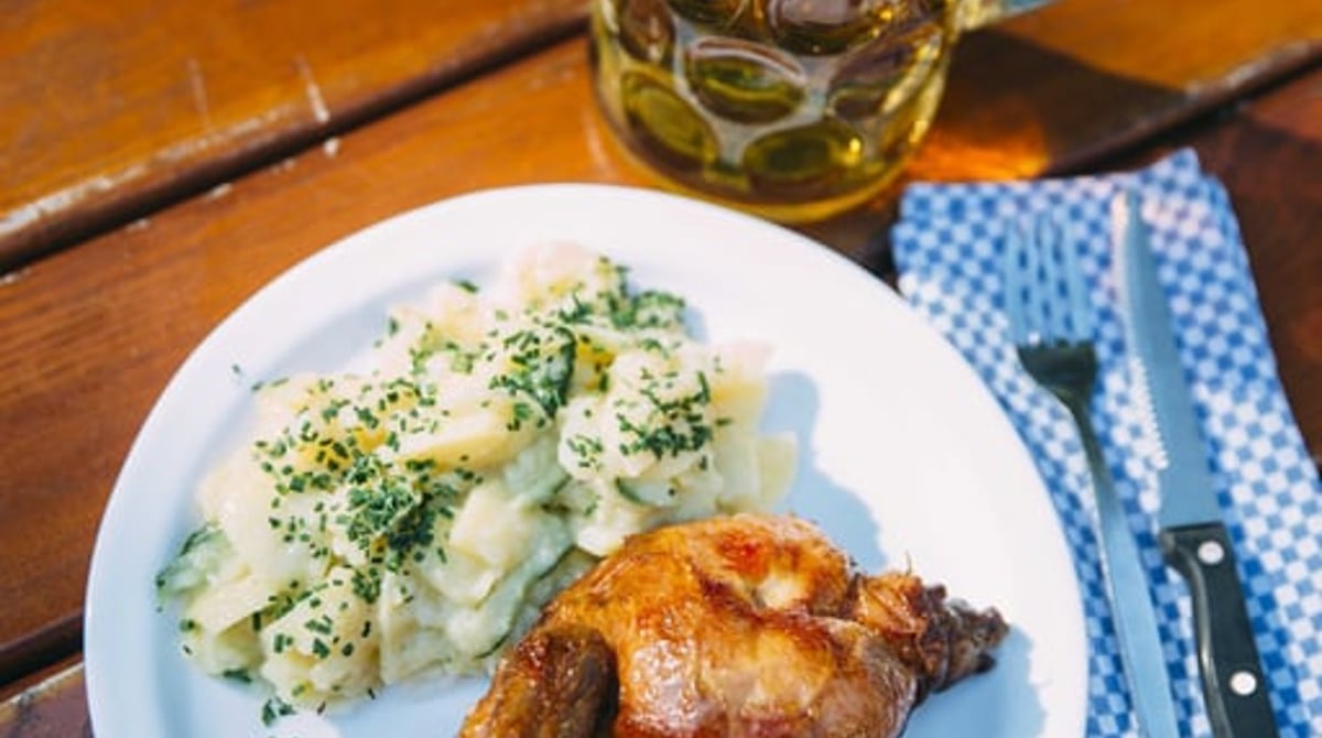 Ein Glas Bier und ein halbes Hendl mit Kartoffelsalat auf einem Holztisch