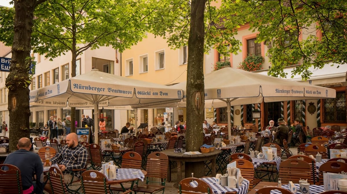 Biergarten des Bratwurst Glöckl am Dom mit Tischen unter Bäumen und Sonnenschirmen am Frauenplatz