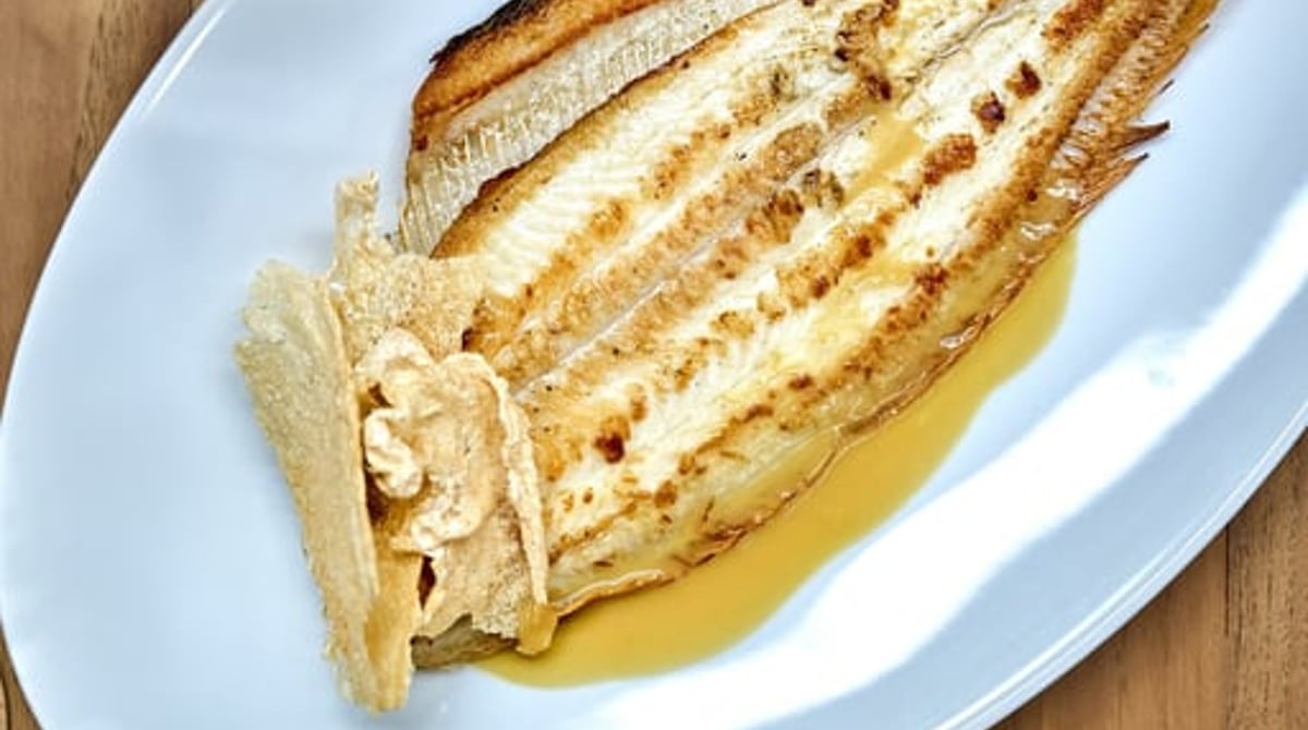 Im Ganzen gegrillte Seezunge mit Buttersauce auf einer ovalen Platte