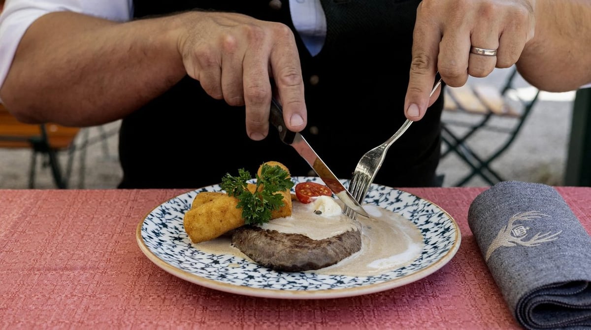 Ein Gericht wird auf einem Teller an einem gedeckten Tisch im Königlichen Hirschgarten angeschnitten