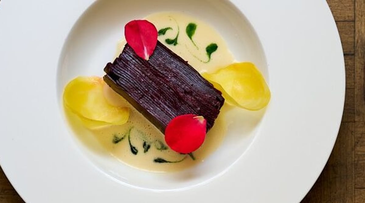 Dunkles Gericht in gelber Sauce mit Rosenblättern auf einem weißen Teller