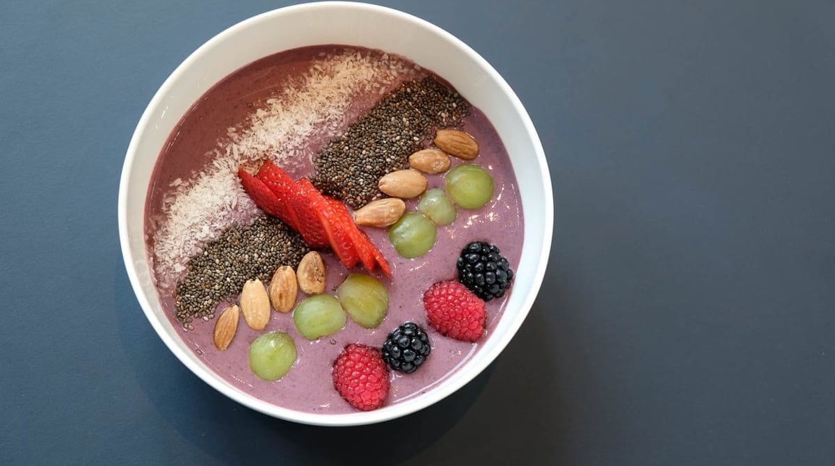 Schale mit Açai-Bowl, garniert mit Beeren, Mandeln, Trauben und Chiasamen