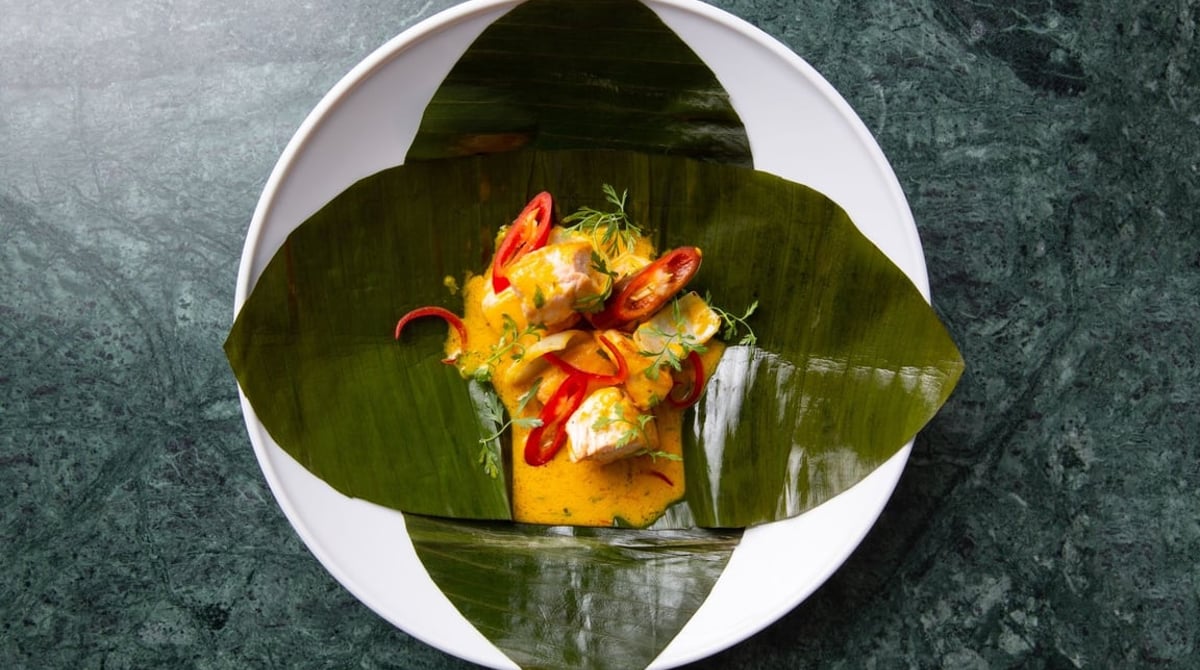 Ceviche Caliente im Bananenblatt auf einem weißen Teller vor grünem Marmor