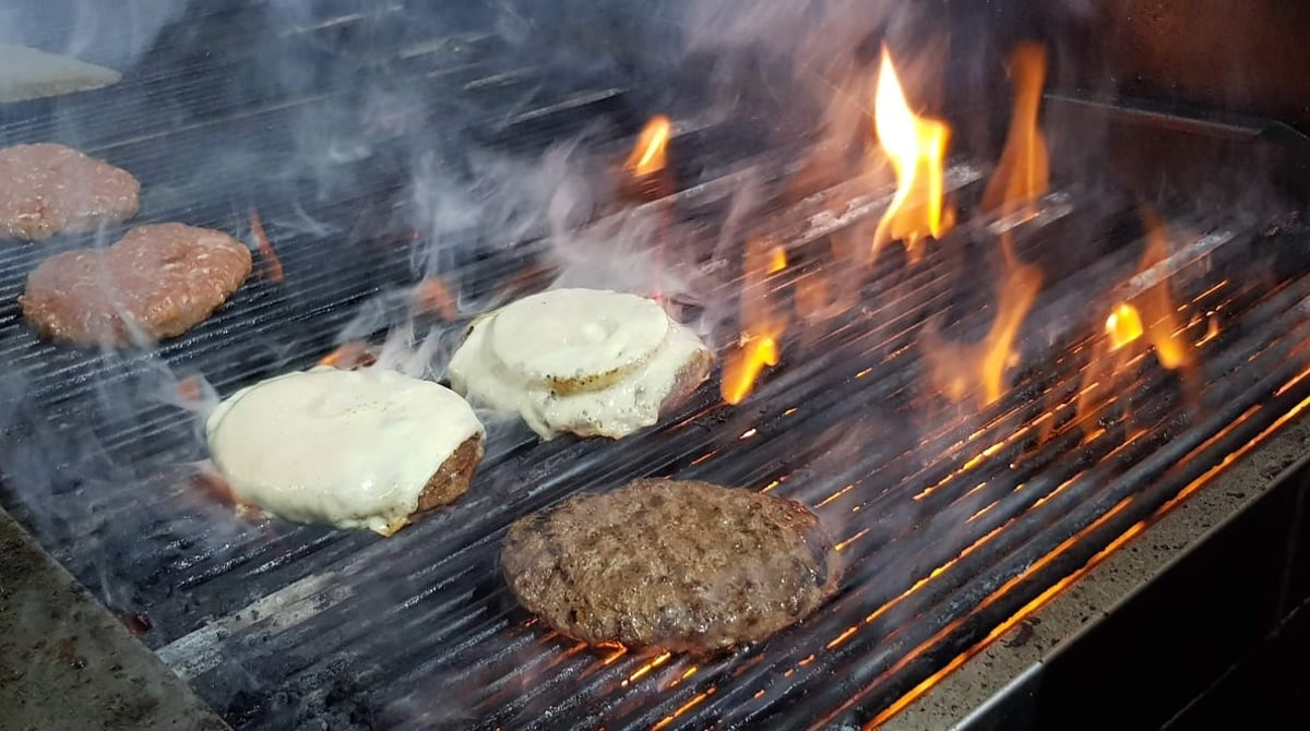 Patties und Burgerbrötchen mit Käse auf dem Grill über offener Flamme