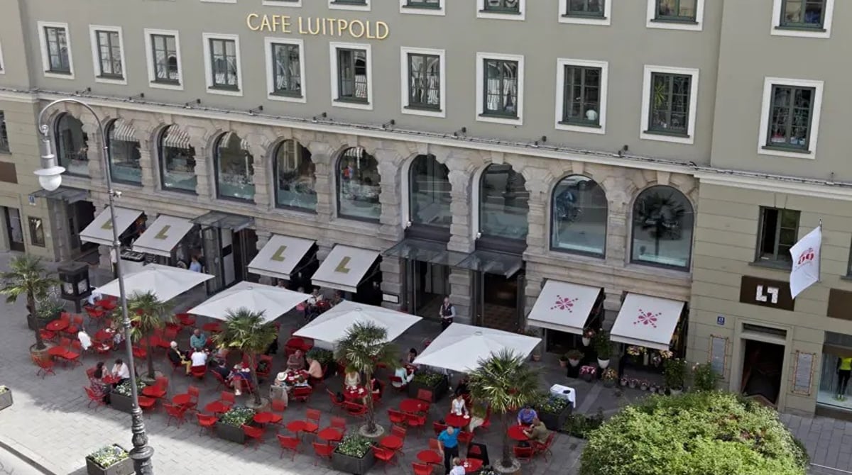 Fassade des Café Luitpold an der Brienner Straße mit Terrasse, Sonnenschirmen und roten Stühlen