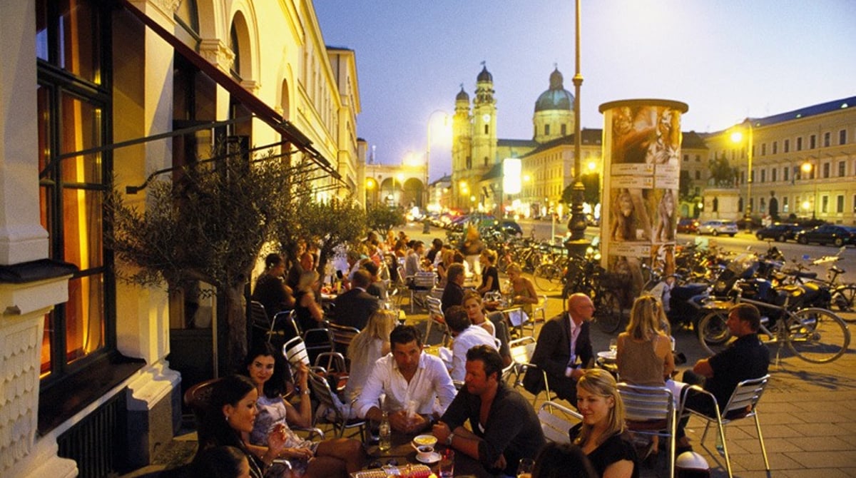 Gäste draußen vor Schumann's Bar am Abend, im Hintergrund eine Kirche mit Kuppel