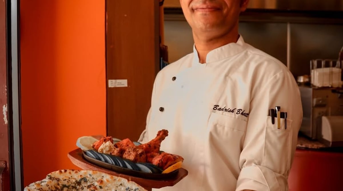 Koch hält einen Teller mit Naan und gegrillten Spießen