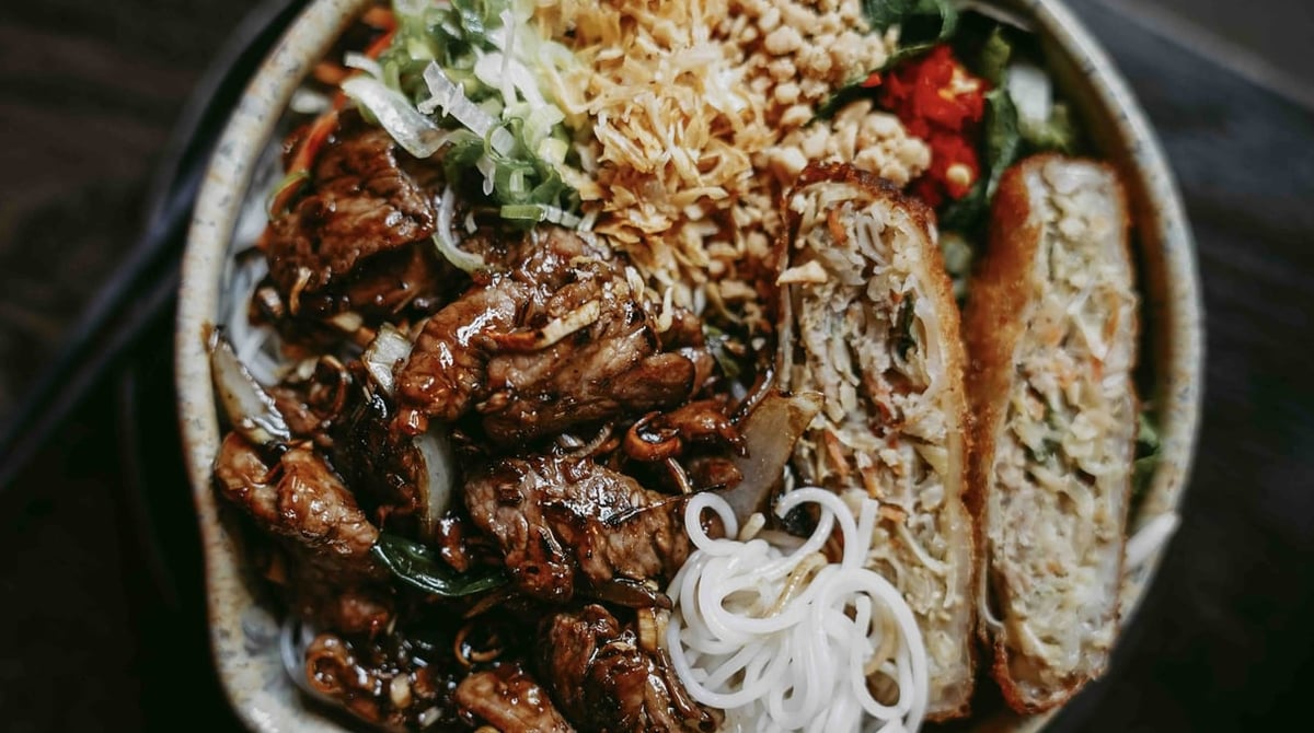 Schale mit mariniertem Fleisch, Reisnudeln, Knuspertopping und aufgeschnittener Frühlingsrolle