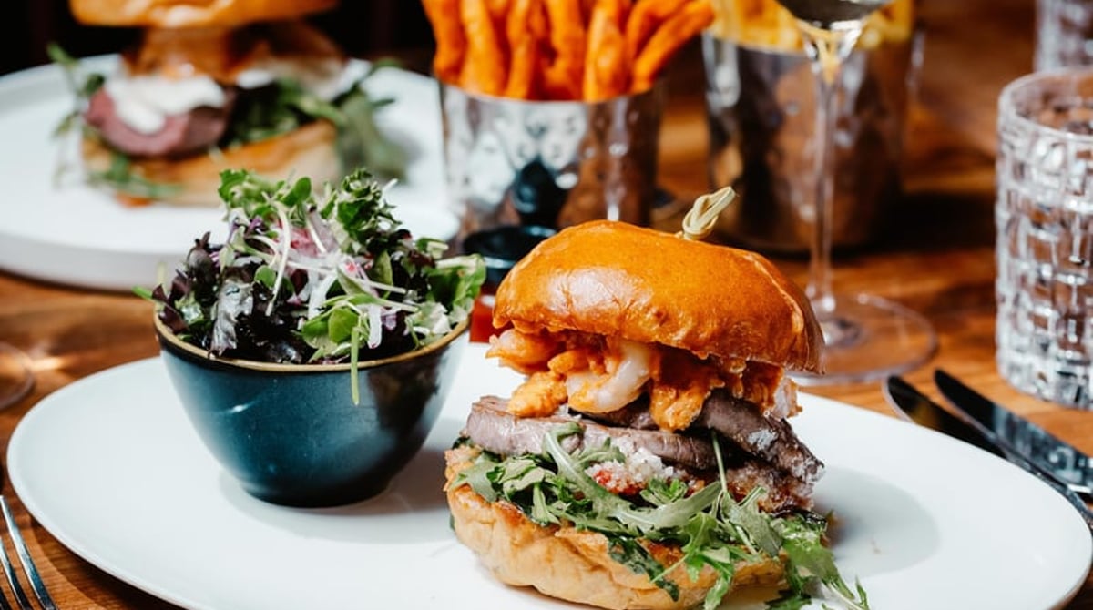 Surf & Turf Burger mit Salat und Süßkartoffel-Pommes, dahinter Weißwein
