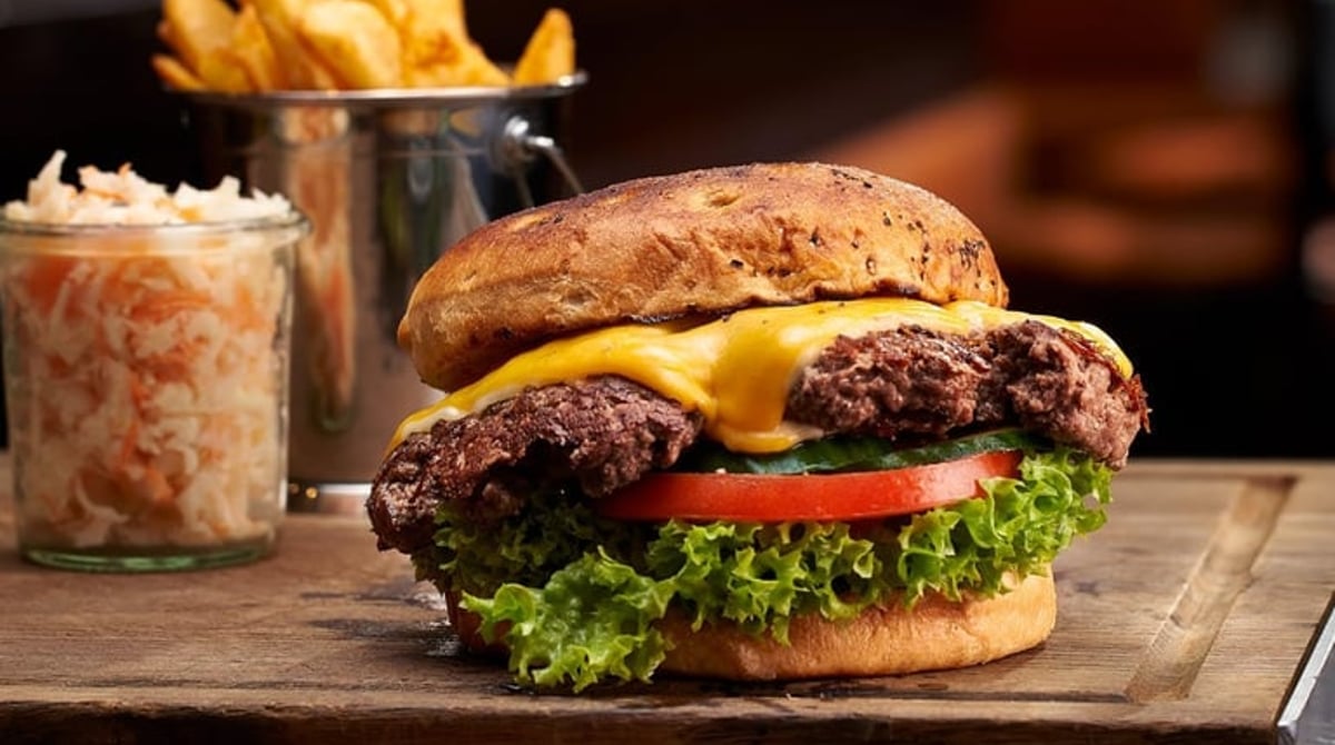 Cheeseburger mit Cheddar, Salat und Tomate, im Hintergrund die Bar der Drunken Cow