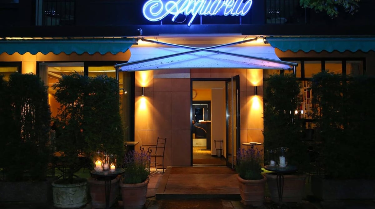 Beleuchteter Eingang des Restaurants Acquarello mit Leuchtschrift am Abend