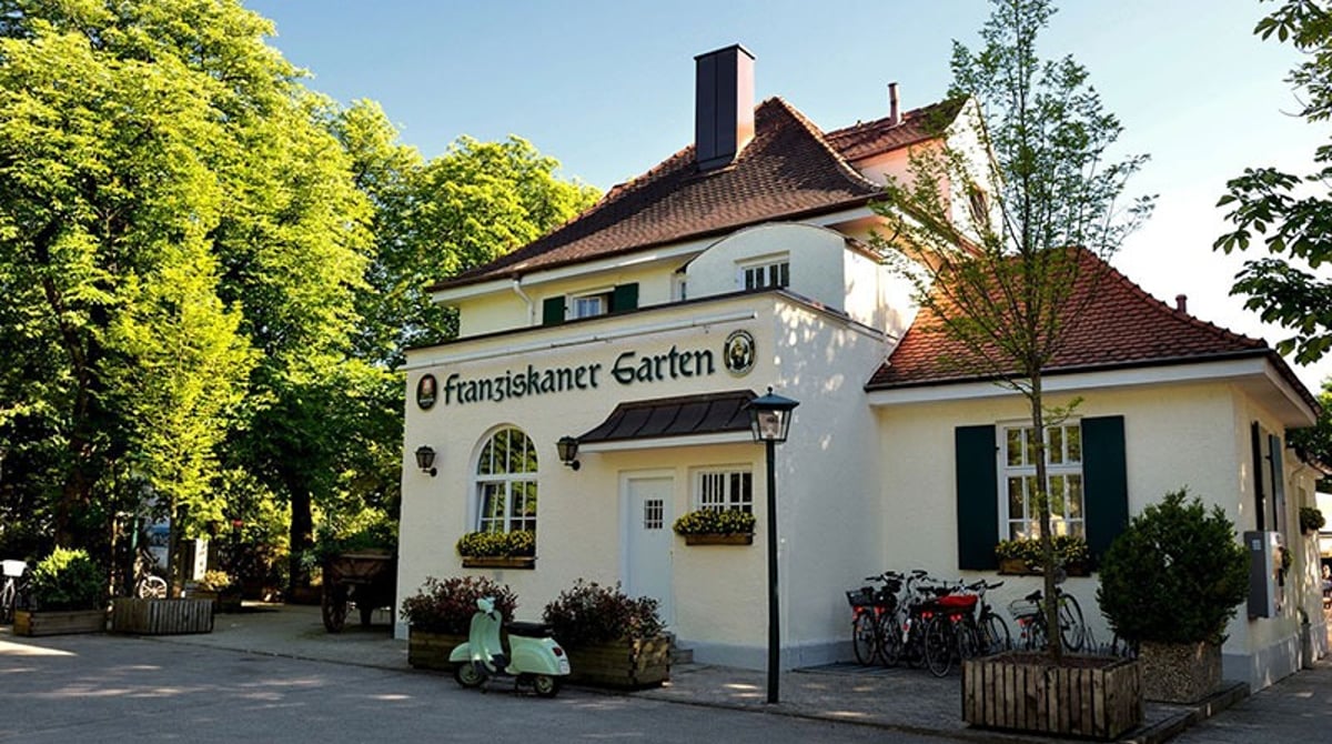 Gelbes Wirtshaus-Gebäude des Franziskaner Garten in Trudering mit Schriftzug an der Fassade und Bäumen davor